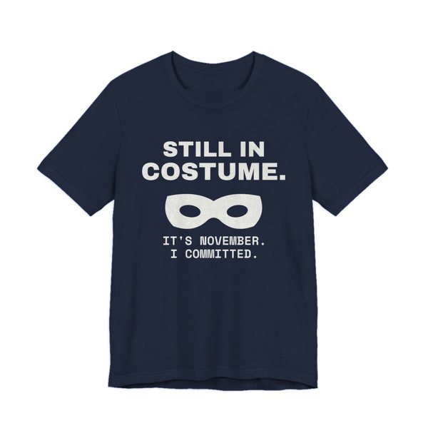 Navy t-shirt printed in off-white ink with “Still in Costume.” above an eye mask, with “It's November. I committed.”