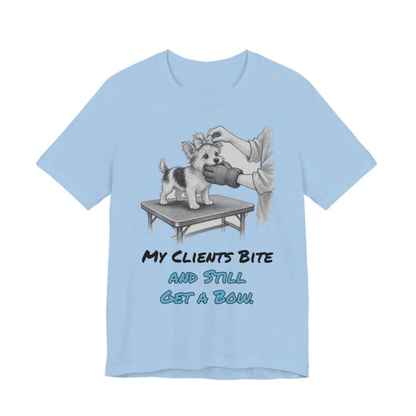 Baby Blue t-shirt printed in full-color print with a full-color pencil drawing of a small dog getting a bow on a grooming table, nipping at the groomer's glove and the words “My Clients Bite and Still Get a Bow.”