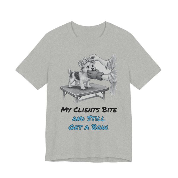 Athletic Heather t-shirt printed in full-color print with a full-color pencil drawing of a small dog getting a bow on a grooming table, nipping at the groomer's glove and the words “My Clients Bite and Still Get a Bow.”