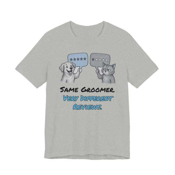 Athletic Heather t-shirt printed in full-color print with a full-color pencil drawing of a dog holding a five-star review and a cat holding a one-star review and the words “Same Groomer. Very Different Reviews.”