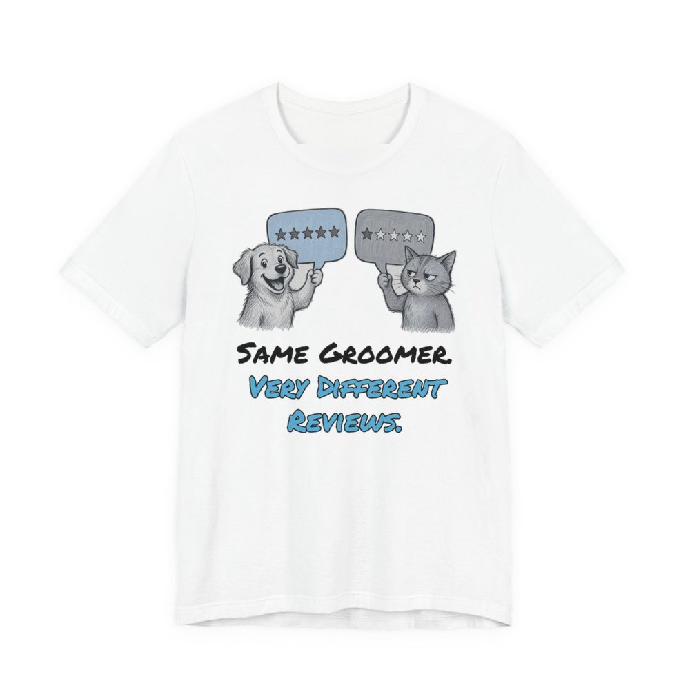 White t-shirt printed in full-color print with a full-color pencil drawing of a dog holding a five-star review and a cat holding a one-star review and the words “Same Groomer. Very Different Reviews.”