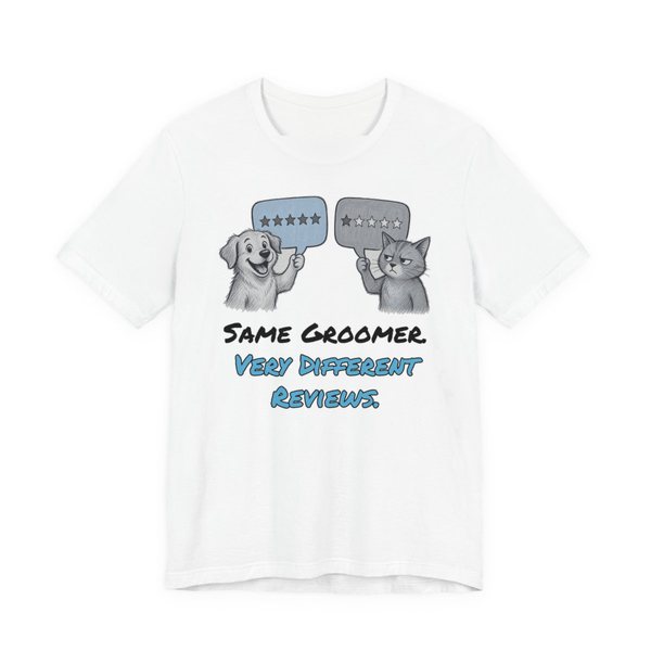 White t-shirt printed in full-color print with a full-color pencil drawing of a dog holding a five-star review and a cat holding a one-star review and the words “Same Groomer. Very Different Reviews.”