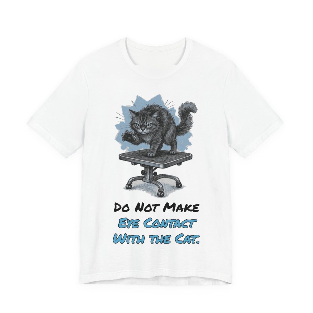White t-shirt printed in full-color print with a full-color pencil drawing of an angry cat on a grooming table and the words “Do Not Make Eye Contact With the Cat.”
