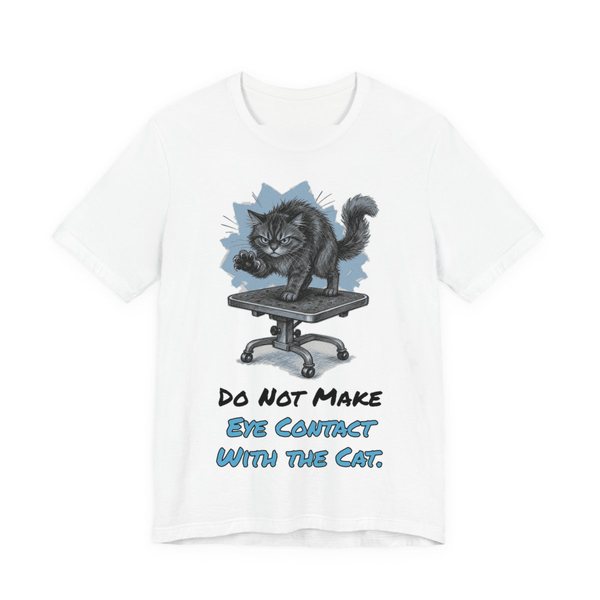White t-shirt printed in full-color print with a full-color pencil drawing of an angry cat on a grooming table and the words “Do Not Make Eye Contact With the Cat.”