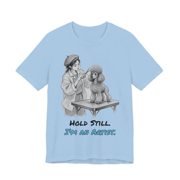 Baby Blue t-shirt printed in full-color print with a full-color pencil drawing of a groomer in a beret sculpting a poodle cut and the words “Hold Still. I'm an Artist.”