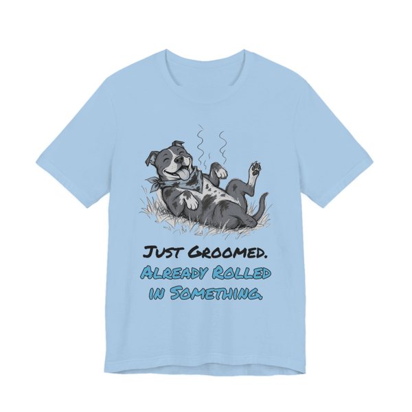 Baby Blue t-shirt printed in full-color print with a full-color pencil drawing of a freshly groomed pit bull with a bandana rolling in the grass and the words “Just Groomed. Already Rolled in Something.”