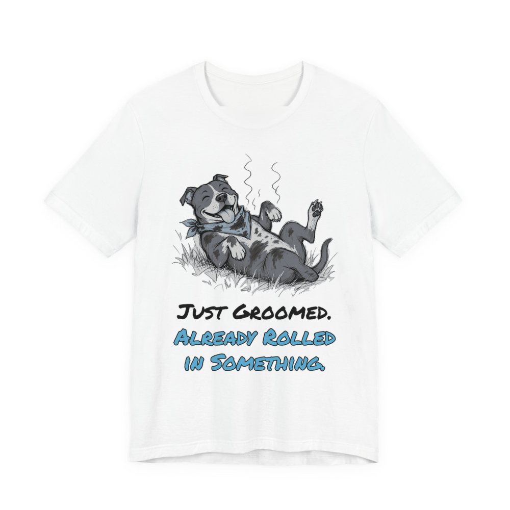 White t-shirt printed in full-color print with a full-color pencil drawing of a freshly groomed pit bull with a bandana rolling in the grass and the words “Just Groomed. Already Rolled in Something.”