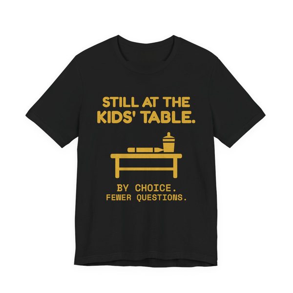 Black t-shirt printed in gold ink with the words “Still at the Kids' Table.”