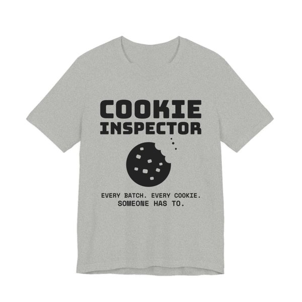 Athletic Heather t-shirt printed in dark ink with a bitten cookie and the words “Cookie Inspector. Every batch. Every cookie. Someone has to.”