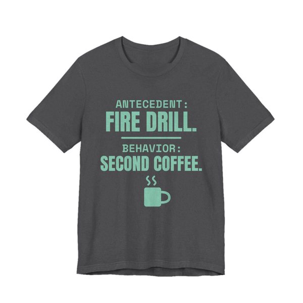 Dark Grey Heather t-shirt printed in chalk mint ink with a steaming mug and the words “Antecedent: Fire Drill. Behavior: Second Coffee.”