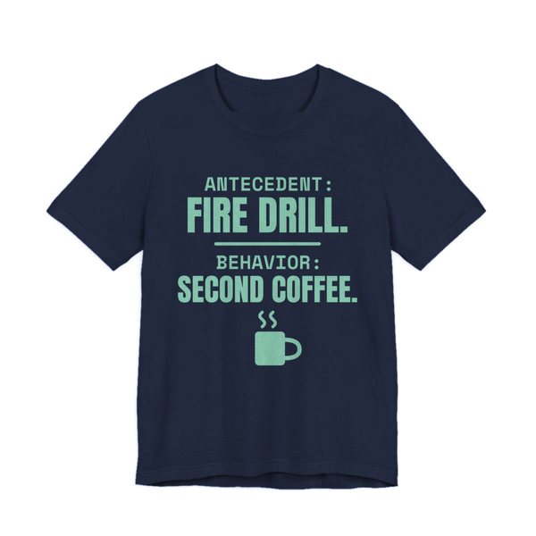 Navy t-shirt printed in chalk mint ink with a steaming mug and the words “Antecedent: Fire Drill. Behavior: Second Coffee.”