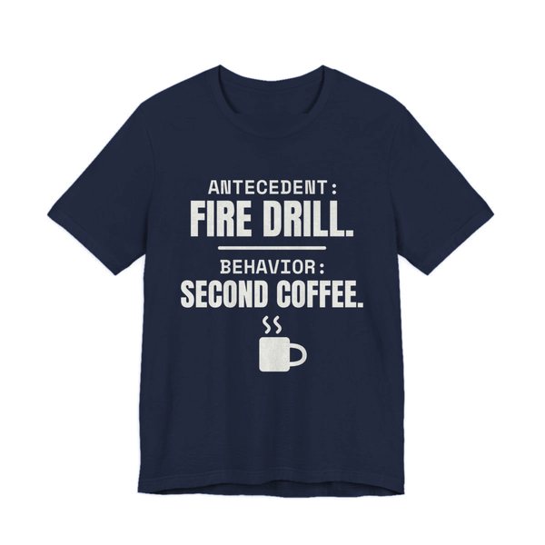 Navy t-shirt printed in off-white ink with a steaming mug and the words “Antecedent: Fire Drill. Behavior: Second Coffee.”