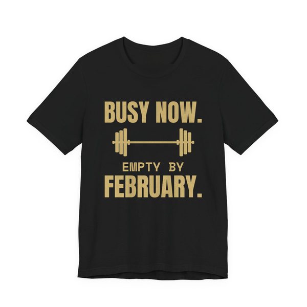 Black t-shirt printed in champagne gold ink with a barbell and the words “Busy Now. Empty by February.”