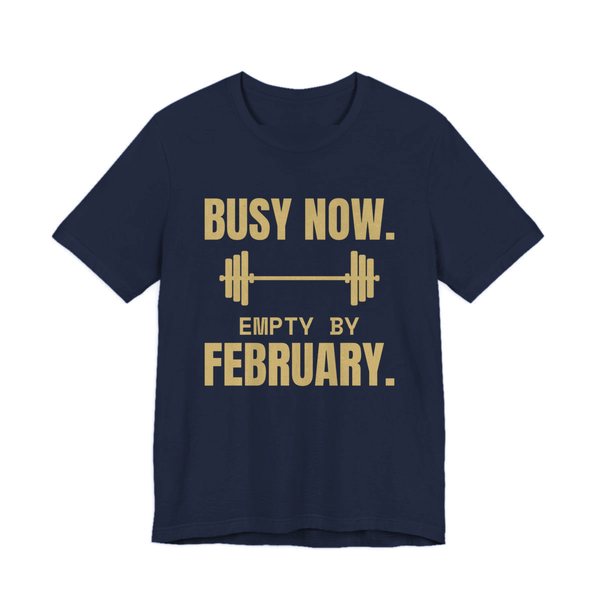 Navy t-shirt printed in champagne gold ink with a barbell and the words “Busy Now. Empty by February.”