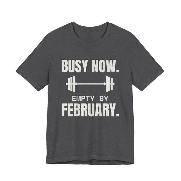 Dark Grey Heather t-shirt printed in off-white ink with a barbell and the words “Busy Now. Empty by February.”