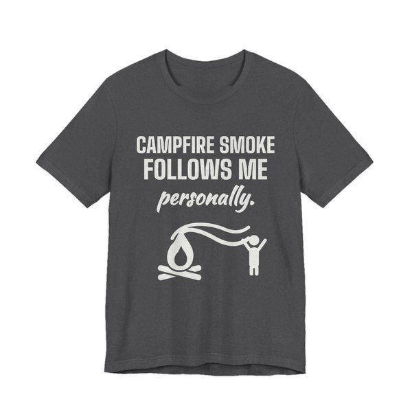 Dark Grey Heather t-shirt printed in off-white ink with a campfire whose smoke trails after a little stick figure and the words “Campfire Smoke Follows Me Personally.”