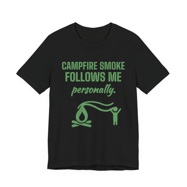 Black t-shirt printed in pine green ink with a campfire whose smoke trails after a little stick figure and the words “Campfire Smoke Follows Me Personally.”