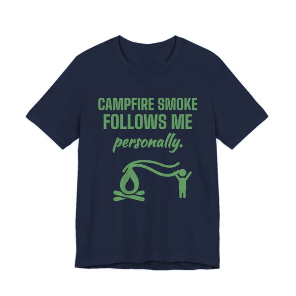 Navy t-shirt printed in pine green ink with a campfire whose smoke trails after a little stick figure and the words “Campfire Smoke Follows Me Personally.”