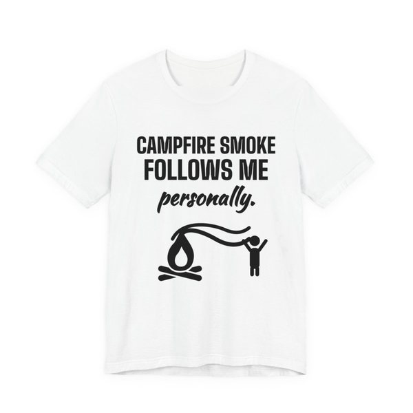 White t-shirt printed in dark ink with a campfire whose smoke trails after a little stick figure and the words “Campfire Smoke Follows Me Personally.”