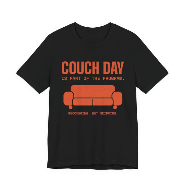 Black t-shirt printed in orange ink with a couch and the words “Couch Day Is Part of the Program. Recovering, Not Skipping.”