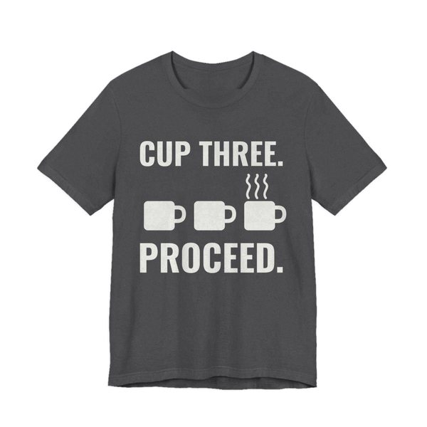 Dark Grey Heather t-shirt printed in off-white ink with a row of mugs, the last one steaming, and the words “Cup Three. Proceed.”