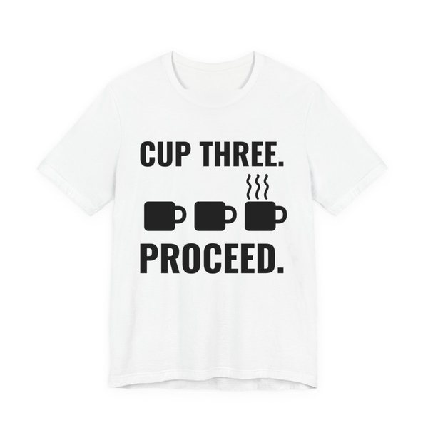White t-shirt printed in dark ink with a row of mugs, the last one steaming, and the words “Cup Three. Proceed.”