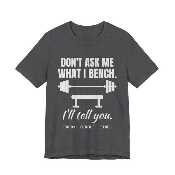 Dark Grey Heather t-shirt printed in off-white ink with a barbell over a bench and the words “Don't Ask Me What I Bench. I'll Tell You. Every. Single. Time.”