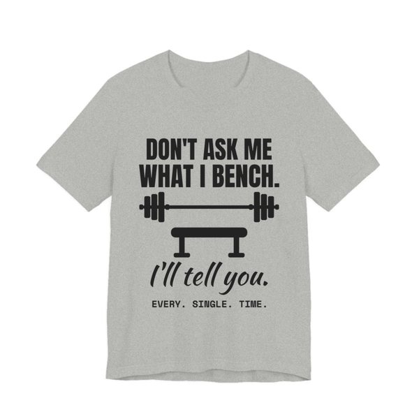 Athletic Heather t-shirt printed in dark ink with a barbell over a bench and the words “Don't Ask Me What I Bench. I'll Tell You. Every. Single. Time.”