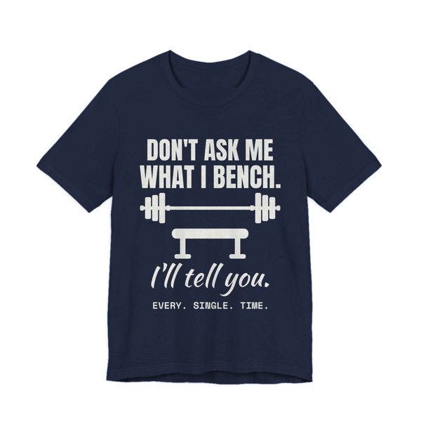 Navy t-shirt printed in off-white ink with a barbell over a bench and the words “Don't Ask Me What I Bench. I'll Tell You. Every. Single. Time.”
