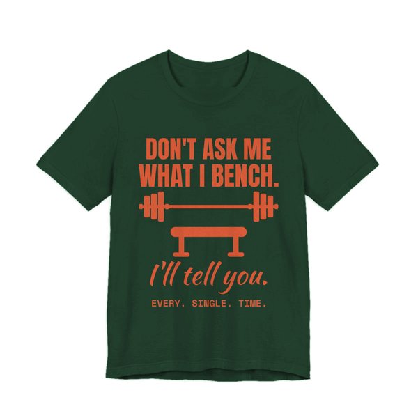 Forest t-shirt printed in orange ink with a barbell over a bench and the words “Don't Ask Me What I Bench. I'll Tell You. Every. Single. Time.”