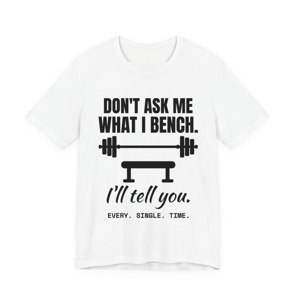 White t-shirt printed in dark ink with a barbell over a bench and the words “Don't Ask Me What I Bench. I'll Tell You. Every. Single. Time.”