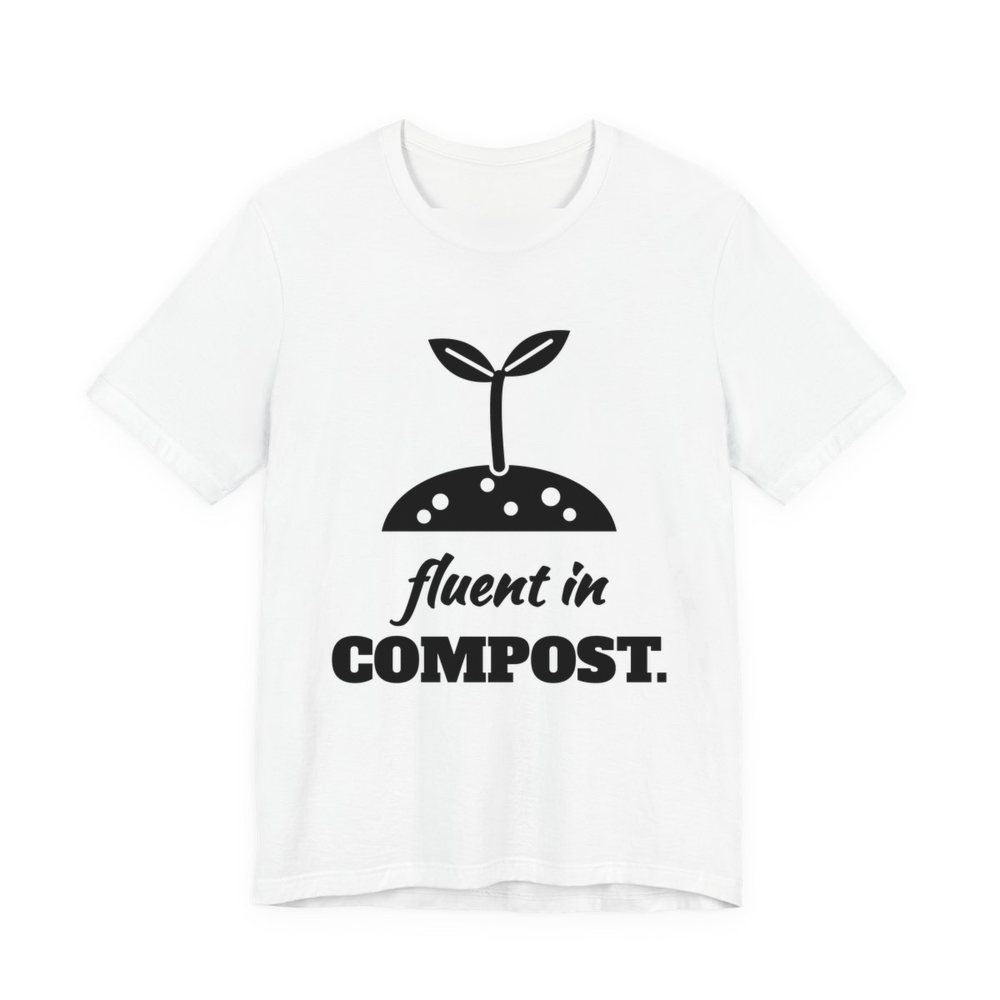 White t-shirt printed in dark ink with a sprout in a mound of soil and the words “Fluent in Compost.”