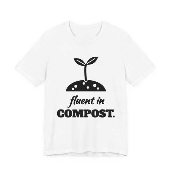 White t-shirt printed in dark ink with a sprout in a mound of soil and the words “Fluent in Compost.”