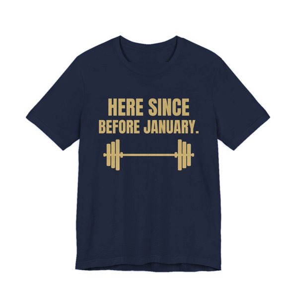 Navy t-shirt printed in champagne gold ink with a barbell and the words “Here Since Before January.”
