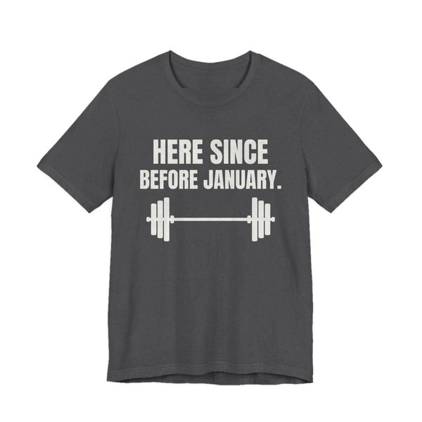 Dark Grey Heather t-shirt printed in off-white ink with a barbell and the words “Here Since Before January.”