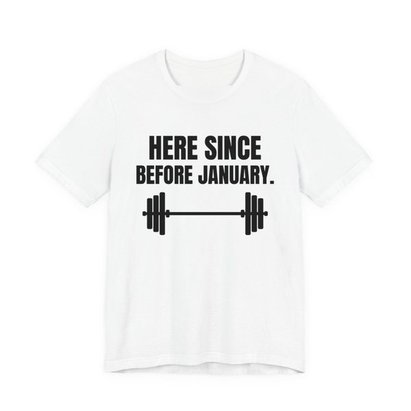 White t-shirt printed in dark ink with a barbell and the words “Here Since Before January.”