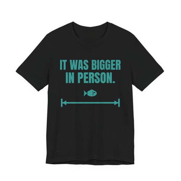 Black t-shirt printed in teal ink with a small fish on a long measuring arrow and the words “It Was Bigger in Person.”
