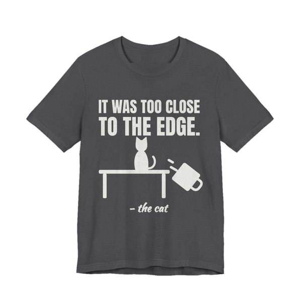 Dark Grey Heather t-shirt printed in off-white ink with a cat on a table, a falling mug and the words “It Was Too Close to the Edge.”