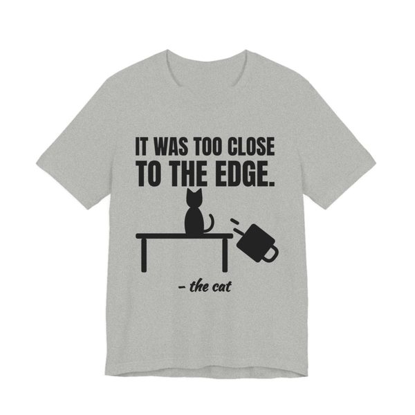 Athletic Heather t-shirt printed in dark ink with a cat on a table, a falling mug and the words “It Was Too Close to the Edge.”