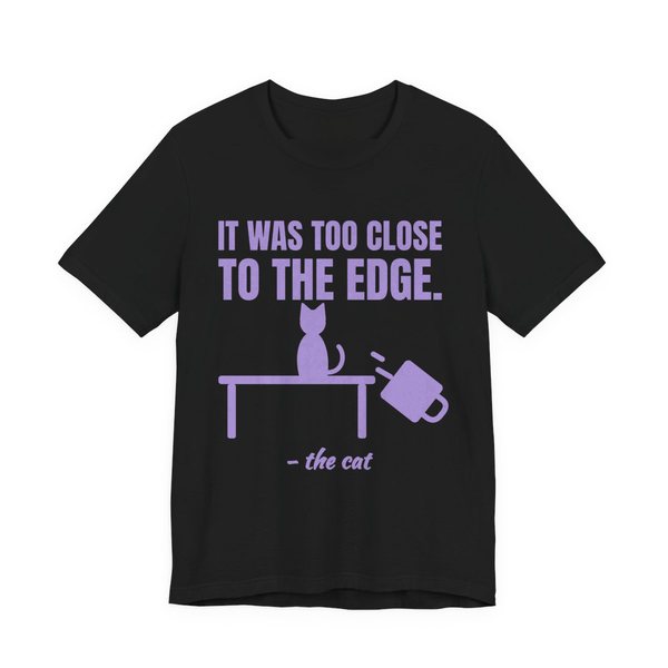 Black t-shirt printed in lavender ink with a cat on a table, a falling mug and the words “It Was Too Close to the Edge.”