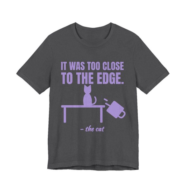 Dark Grey Heather t-shirt printed in lavender ink with a cat on a table, a falling mug and the words “It Was Too Close to the Edge.”