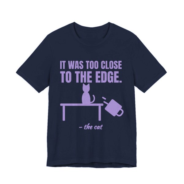 Navy t-shirt printed in lavender ink with a cat on a table, a falling mug and the words “It Was Too Close to the Edge.”