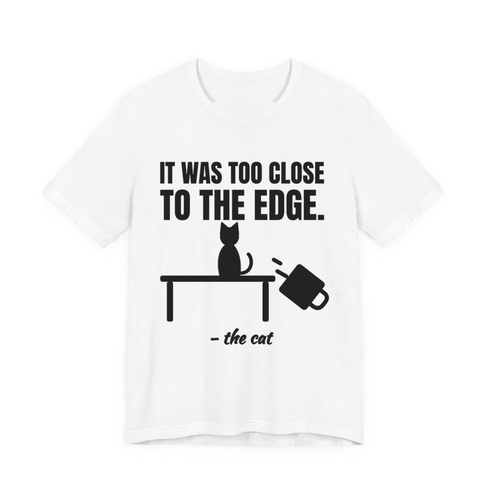 White t-shirt printed in dark ink with a cat on a table, a falling mug and the words “It Was Too Close to the Edge.”