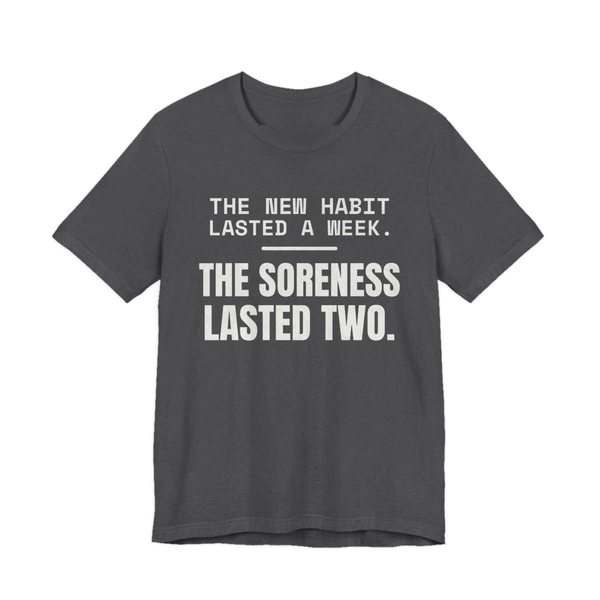 Dark Grey Heather t-shirt printed in off-white ink with the words “New Habit Lasted a Week. The Soreness Lasted Two.”