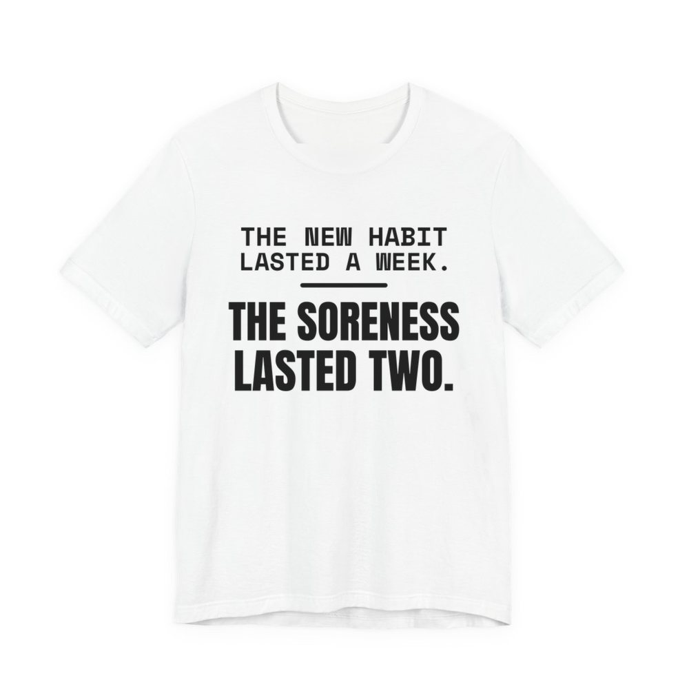White t-shirt printed in dark ink with the words “New Habit Lasted a Week. The Soreness Lasted Two.”