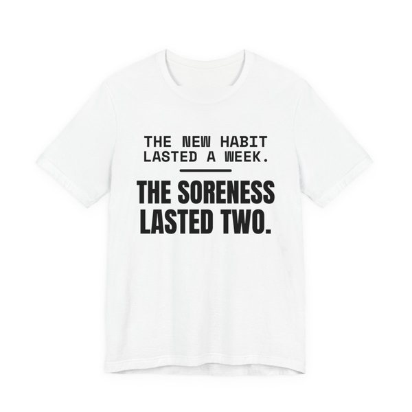 White t-shirt printed in dark ink with the words “New Habit Lasted a Week. The Soreness Lasted Two.”