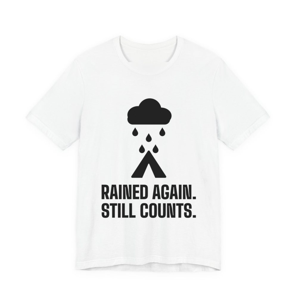White t-shirt printed in dark ink with a rain cloud over a tent and the words “Rained Again. Still Counts.”