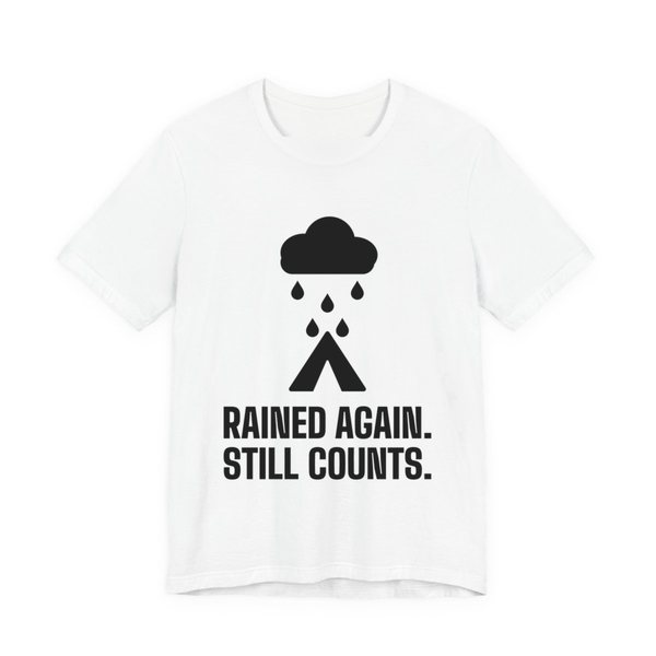 White t-shirt printed in dark ink with a rain cloud over a tent and the words “Rained Again. Still Counts.”