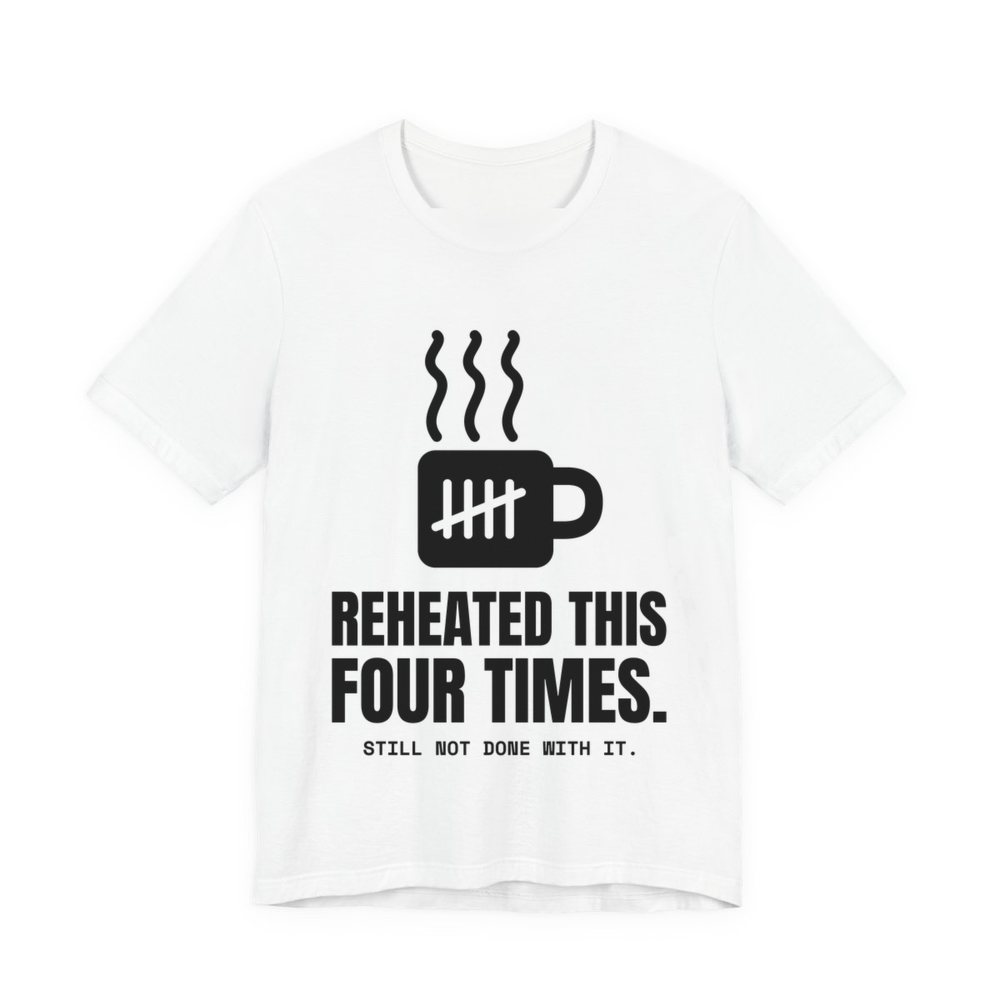 White t-shirt printed in dark ink with a mug with tally marks and the words “Reheated This Four Times.”
