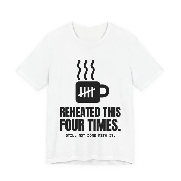 White t-shirt printed in dark ink with a mug with tally marks and the words “Reheated This Four Times.”